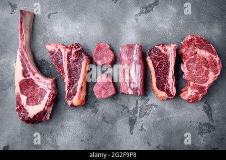 Vari tagli di carne di manzo marmorizzata e bistecche stagionate secche, tomahawk, t bone, bistecca club, costolette e tagli di filetto, su sfondo grigio in pietra, vista dall'alto Foto Stock