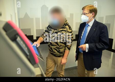 Herford, Germania. 11 Giugno 2021. Un prigioniero della JVA (l-r) e Peter Biesenbach (CDU), ministro della Giustizia della NRW, si trovano accanto a un terminale di informazione nel centro di detenzione giovanile della prigione di Herford. Lo strumento sta lanciando un progetto pilota sulla digitalizzazione nel sistema correttiva giovanile. Credit: Frito Gentsch/dpa - ATTENZIONE: La persona è stata pixelata per motivi legali/dpa/Alamy Live News Foto Stock