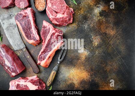 Set di bistecche fresche di manzo marmorizzato grezzo, tomahawk, t bone, bistecca club, costolette e tagli di filetto, su vecchio sfondo rustico scuro, vista dall'alto piatto Foto Stock