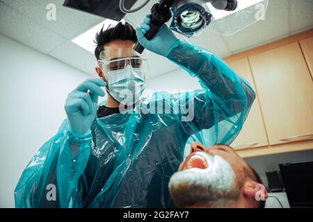 Paziente maschio caucasico seduto in ufficio medici mentre l'infermiere esamina l'interno della bocca Foto Stock