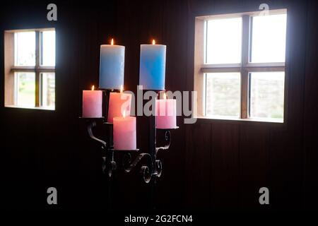 Standaard con candele colorate in cabina di legno con luce del giorno che brilla attraverso le finestre Foto Stock