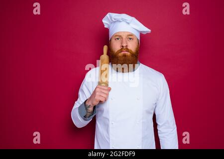 chef serio con barba e grembiule rosso chef tiene in legno rolling pin Foto Stock