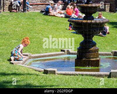 Giovane ragazza che gioca in una fontana pubblica al triangolo di Bude, Cornovaglia, Regno Unito Foto Stock