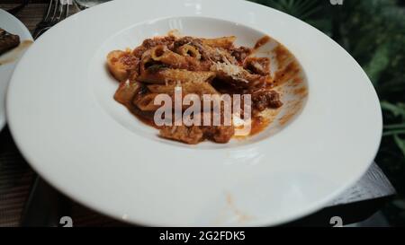 Mezza Pasta italiana mangiata con salsa di pomodoro e parmigiano su un piatto bianco mangiando fuori sedersi fuori cena informale manca un morso Foto Stock