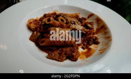 Mezza Pasta italiana mangiata con salsa di pomodoro e parmigiano su un piatto bianco mangiando fuori sedersi fuori cena informale manca un morso Foto Stock