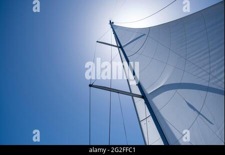 Vela con il vento a mare aperto, concetto di vacanze estive. Vele riempite di vento da yacht su sfondo blu chiaro del cielo. Guardando verso il cielo, sole shi Foto Stock