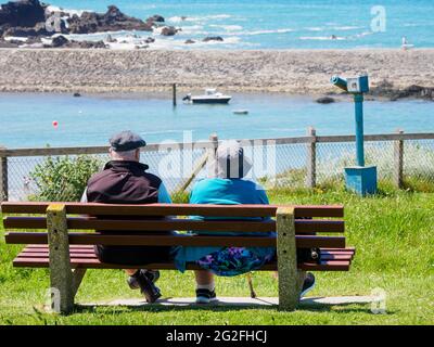 L'uomo anziano e la donna si sedettero su una panchina pubblica che guardava verso il mare, Bude, Cornovaglia, Regno Unito Foto Stock