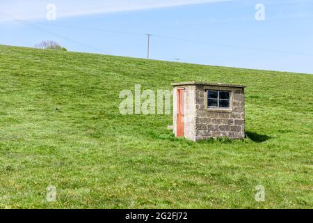 Stazione di pompaggio di mattoni accanto ad un pozzo in una cavità nel mezzo di un campo. Foto Stock