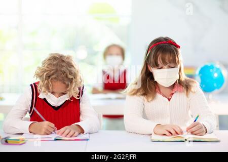 Bambini in maschera facciale in classe scolastica. Il bambino torna a scuola dopo il blocco del coronavirus. Bambino primario nella pandemia di covid-19. Prevenzione della diffusione dei virus. Foto Stock