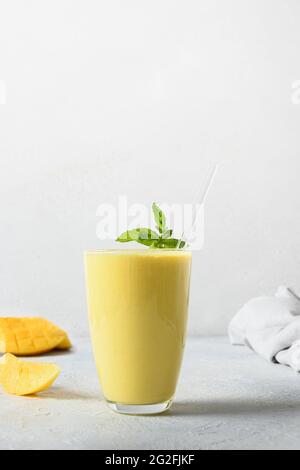 Mango indiano lassi su sfondo bianco. Verticale. Bevanda ayurvedica con mango. Freschezza lassi fatto di yogurt, acqua, spezie, frutta e ghiaccio. Foto Stock