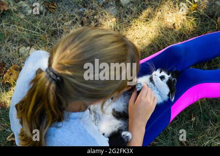 Defocus bambina bionda che gioca con gatto, bianco e nero piccolo gattino relax. Natura giallo estate sfondo. Ragazza stroking animale domestico. Ami gli animali Foto Stock