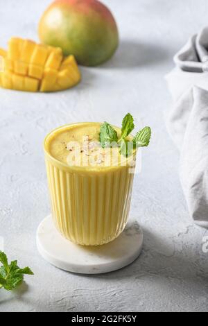 Mango lassi, frullati o frullato su sfondo bianco. Bevanda ayurvedica indiana con mango, yogurt, acqua, spezie, frutta e ghiaccio. Primo piano. Foto Stock