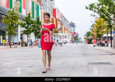 Donna asiatica che cammina nel centro della città sulla via dello shopping di Wangfujing a Pechino, cina, utilizzando l'app per telefono per trovare indicazioni stradali o testo online. Felice donna cinese Foto Stock