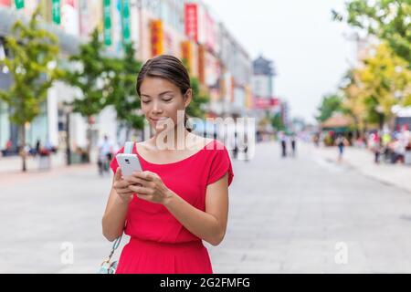 Donna asiatica fuori sulla via dello shopping di Wangfujing a Pechino, cina, utilizzando l'app per il telefono cellulare per fare acquisti online. Happy Chinese Woman che invia SMS su Foto Stock