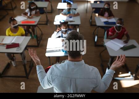 Vista posteriore dell'insegnamento di un insegnante di sesso maschile caucasico nella classe scolastica Foto Stock