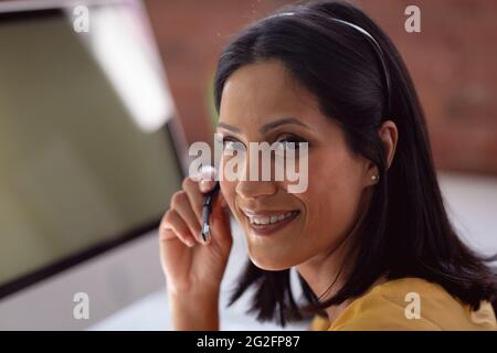 Ritratto di una donna d'affari caucasica felice che indossa una cuffia del telefono seduto alla scrivania girando e sorridendo Foto Stock