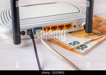 Due banconote da 50 euro e router wireless Wi-Fi bianco con cavi collegati su una scrivania di legno bianco. Concetti di guadagnare soldi in linea, e-commercio. Foto Stock