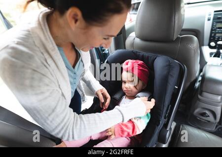 Madre caucasica che mette il suo bambino nel seggiolino di sicurezza dell'automobile Foto Stock