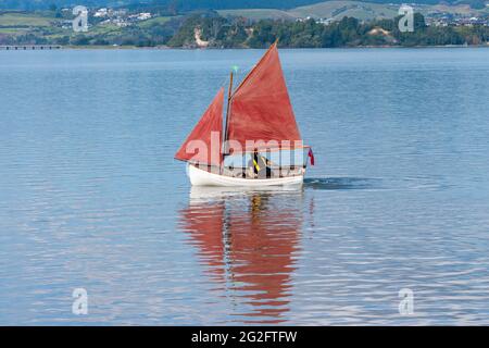 Vele rosse di stile tradizionale su un piccolo yacht becalmed in baia. Foto Stock