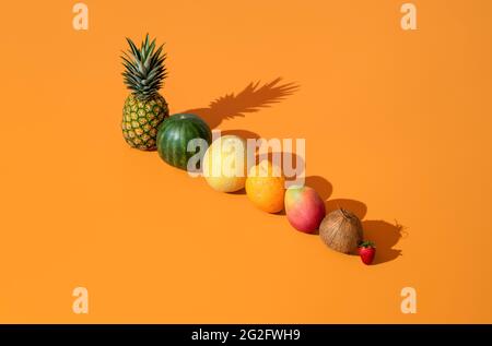 Frutti esotici disposti in fila su un tavolo arancione. Frutta fresca d'estate minimalista in luce brillante, che cade una dura ombra. Foto Stock