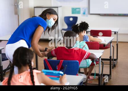 Insegnante di afroamericana che indossa una maschera che insegna il ragazzo afroamericano in classe a scuola Foto Stock