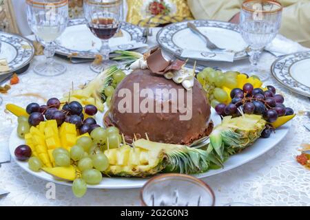 Un piatto di frutta. Mango, uva e ananas. Torta al cioccolato surgelata, piatto fruttato, servita al matrimonio Foto Stock