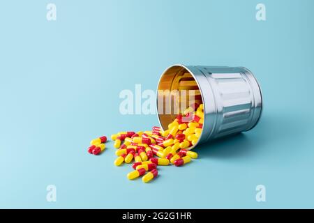 i rifiuti caduti possono pieni di pillole rosse e gialle o compresse su sfondo blu. medicina, farmacia e concetto di coronavirus. copia spazio. Foto Stock