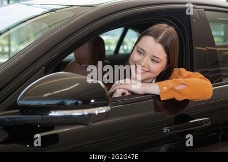 Primo piano di una bella e felice giovane pilota nella sua nuova auto Foto Stock