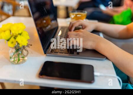 Primo piano foto di un computer portatile femminile che scrive le mani e ricarica lo smartphone sul tavolo Foto Stock