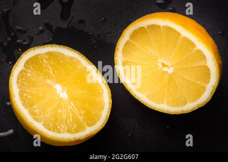 Limone giallo succoso affettato a metà su uno sfondo nero isolato Foto Stock