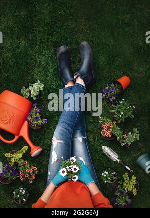 Testa di donna su erba circondata da piante e attrezzi di giardinaggio. Foto Stock