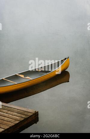 Canoe gialla vuota ad un molo di legno su un lago calmo in Canada. Foto Stock