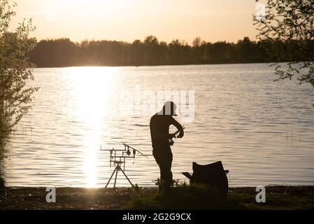 Un pescatore silhouette pesca al tramonto. Foto Stock