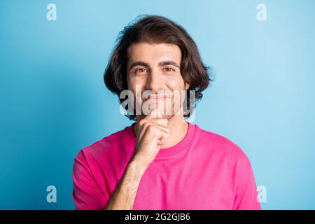 Foto di bel brunetto felice capelli ondulati arabo giovane uomo tenere mano mento indossare t-shirt rosa isolato su sfondo blu Foto Stock