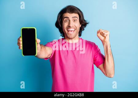 Foto di un tipo di capelli brunetto stupefatto che mostra il telefono per lo sconto pugno su spazio vuoto isolato su sfondo blu colore Foto Stock