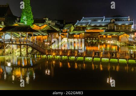 Vista notturna di un ponte piatto in legno che attraversa il canale circondato da tradizionali case cinesi nella storica e panoramica città d'acqua di Wuzhen, in Cina Foto Stock