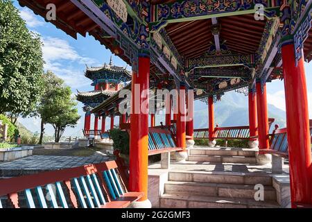 Una passerella coperta in stile cinese di colore rosso e blu con panche di riposo che conduce ad un punto panoramico in Stone Drum Town, Shangri-la, Cina Foto Stock