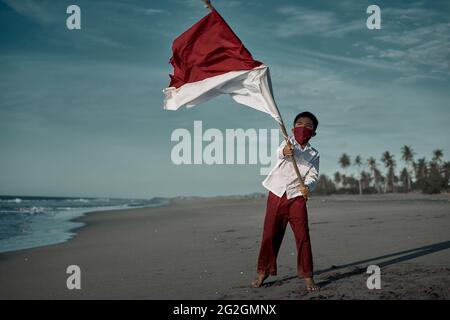 Scolaro in uniforme scolastica con bandiera indonesiana rossa e bianca Foto Stock
