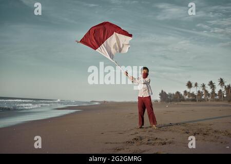 Scolaro in uniforme scolastica con bandiera indonesiana rossa e bianca Foto Stock