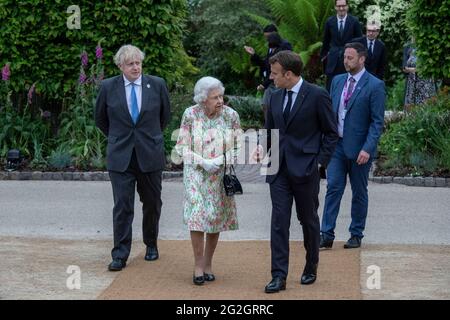 La regina Elisabetta II, parlando con il presidente francese Emmanuel Macron come il primo ministro britannico Boris Johnson guarda sopra, mentre si fanno strada per una foto di gruppo prima di un ricevimento al progetto Eden durante il vertice del G7 in Cornovaglia. Data immagine: Venerdì 11 giugno 2021. Foto Stock