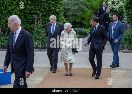 La regina Elisabetta II, parlando con il presidente francese Emmanuel Macron come il primo ministro britannico Boris Johnson guarda sopra, mentre si fanno strada per una foto di gruppo prima di un ricevimento al progetto Eden durante il vertice del G7 in Cornovaglia. Data immagine: Venerdì 11 giugno 2021. Foto Stock