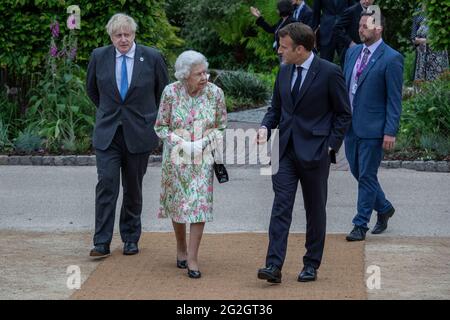 La regina Elisabetta II, parlando con il presidente francese Emmanuel Macron come il primo ministro britannico Boris Johnson guarda sopra, mentre si fanno strada per una foto di gruppo prima di un ricevimento al progetto Eden durante il vertice del G7 in Cornovaglia. Data immagine: Venerdì 11 giugno 2021. Foto Stock