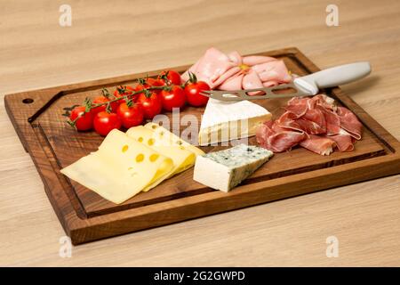 Vista in primo piano di vari tipi di formaggio, carne e pomodori ciliegini su un tagliere di legno Foto Stock