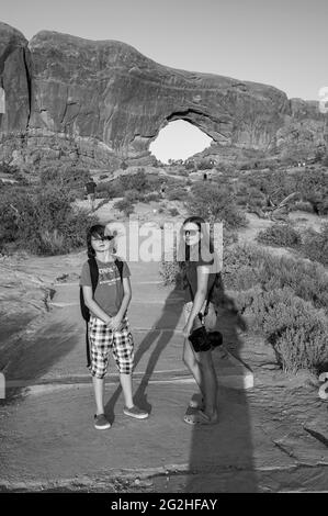 Ragazza e ragazzo di fronte al North Window Arch. Arch sul lato nord delle finestre, una pinna di arenaria con 2 massicce aperture a forma di occhio nel Parco Nazionale di Arches, vicino a Moab nello Utah, USA. Foto Stock