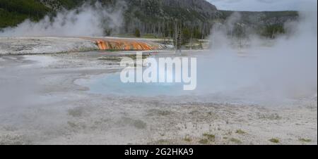 Primavera in Yellowstone: Geyser Spouter del gruppo di smeraldo nella zona del bacino di sabbia nera del bacino superiore del Geyser erutta con il runoff Sunset Lake alle spalle Foto Stock