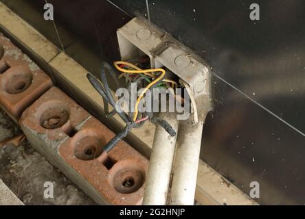 Closeup dei fili elettrici nelle scatole di derivazione scoperte installate sulla parete piastrellata nera vicino al suolo, vista ad angolo alto Foto Stock