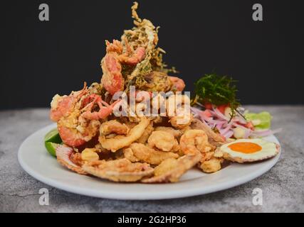 Cibo peruviano: Chicharron de pescado o cracklings di pesce con manioca fritta e insalata di cipolla con peperoncino, servito su un piatto bianco. Messa a fuoco selettiva Foto Stock