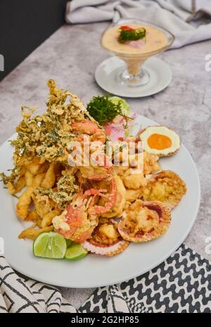 Cibo peruviano: Chicharron de pescado o cracklings di pesce con manioca fritta e insalata di cipolla con peperoncino, servito su un piatto bianco. Messa a fuoco selettiva Foto Stock