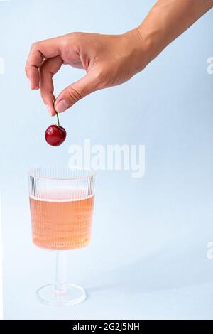 Mano femminile toccare un bicchiere di limonata rosa. Concetto di bevanda estiva. Vita creativa di rinfrescante limonata di bacche e ciliegie. Foto Stock