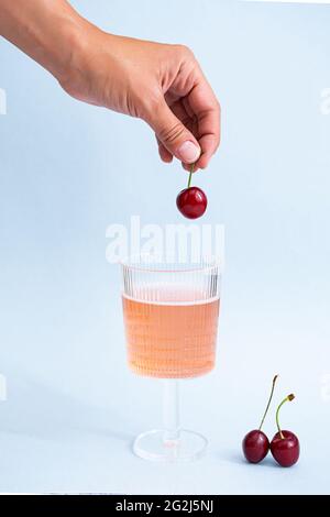 Mano femminile toccare un bicchiere di limonata rosa. Concetto di bevanda estiva. Vita creativa di rinfrescante limonata di bacche e ciliegie. Foto Stock